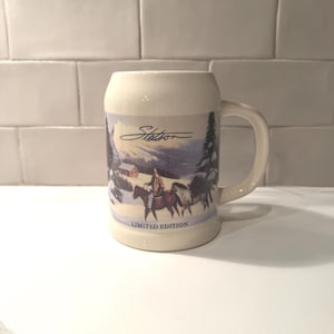 May include: Cream-colored ceramic mug with a handle, featuring a winter scene with a person on horseback and the word "Stetson." The mug also has the words "Limited Edition" printed on it.