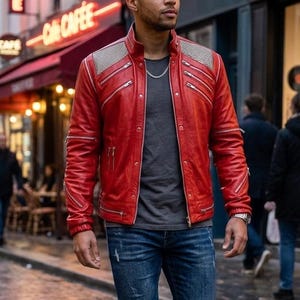 May include: A vibrant red leather jacket featuring a stand-up collar, multiple silver-toned zippered pockets, and textured shoulder panels. The jacket is worn over a plain dark gray t-shirt, paired with blue denim jeans that have distressed details.