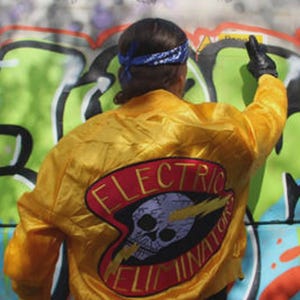 May include: A yellow satin jacket with a large patch on the back that reads "ELECTRIC ELIMINATOR" with a skull and lightning bolt graphic. The person is wearing a blue bandana and black gloves.
