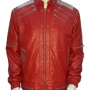 May include: A bright red jacket featuring a stand-up collar, a central silver zipper, and multiple silver-toned zippered pockets across the chest and sleeves. The shoulders are accented with silver metallic panels, and the cuffs are elasticized.