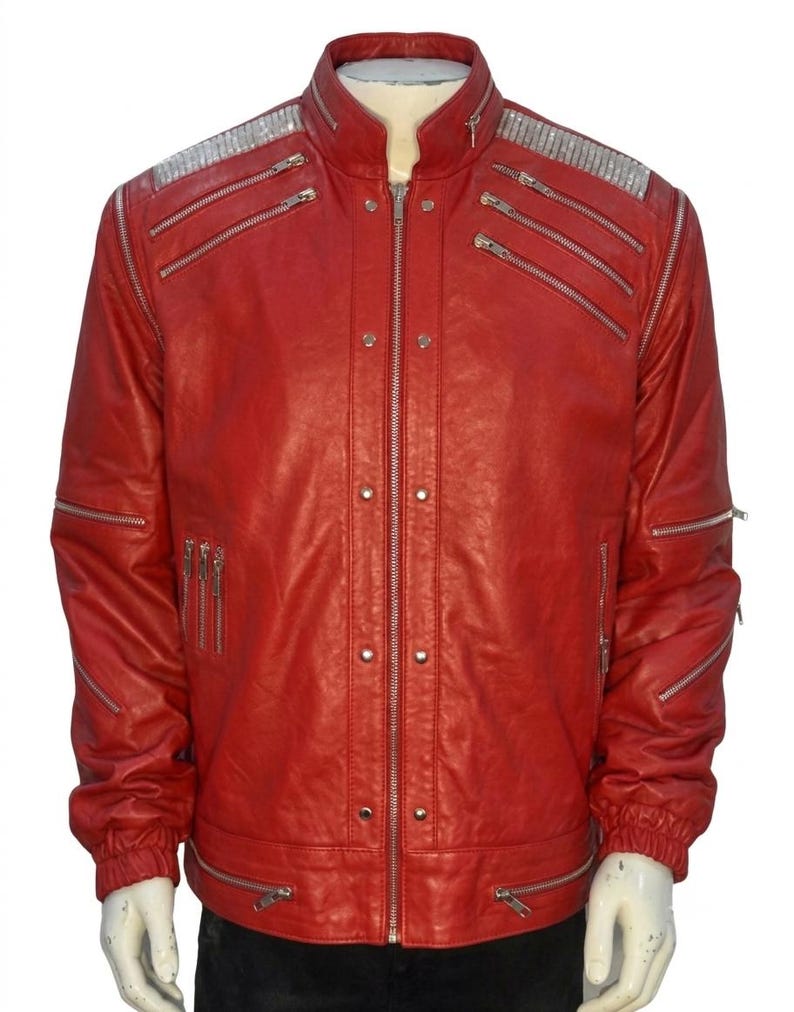 May include: A bright red jacket featuring a stand-up collar, a central silver zipper, and multiple silver-toned zippered pockets across the chest and sleeves. The shoulders are accented with silver metallic panels, and the cuffs are elasticized.