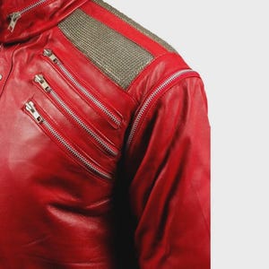 May include: A bright red leather jacket featuring a high collar, silver-toned metal zippers on the chest, and a textured metallic silver panel across the shoulder. The jacket includes a long sleeve and a structured design with multiple zipper closures.
