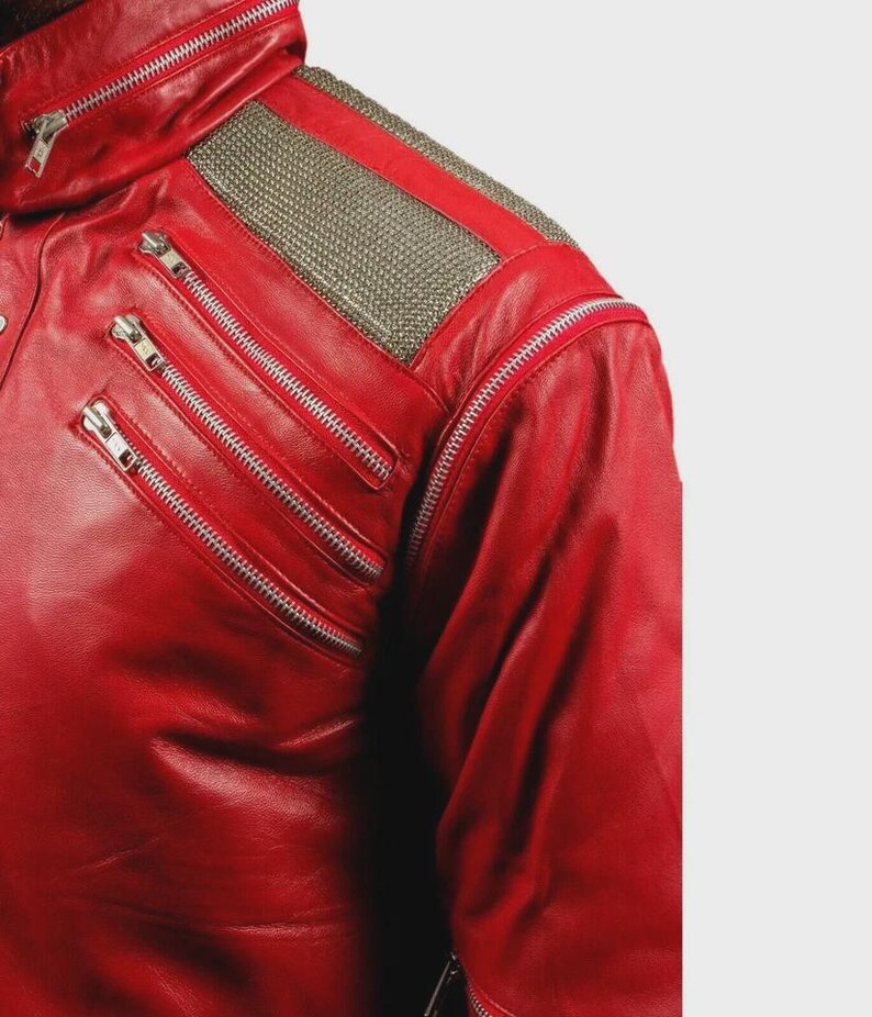 May include: A bright red leather jacket featuring a high collar, silver-toned metal zippers on the chest, and a textured metallic silver panel across the shoulder. The jacket includes a long sleeve and a structured design with multiple zipper closures.