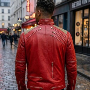 May include: A vibrant red leather jacket featuring a high collar, multiple silver-toned metal zippers across the back and sleeves, and textured gold-toned fabric panels on the shoulders. The jacket has a structured fit with visible seams.