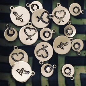 May include: A collection of silver charm pendants with various designs, including hearts, knots, and circles. The charms are all round and have a smooth, polished finish.