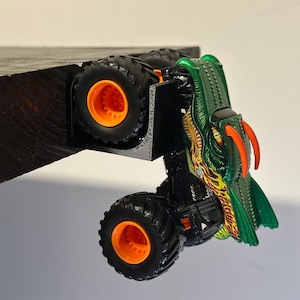 May include: A green and yellow monster truck toy with orange wheels. The truck has a dragon-like design on the front and is black. The tires are large and have a detailed tread pattern.