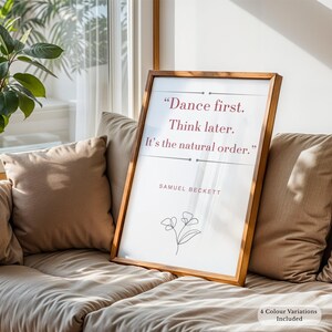 Puede incluir: Un cuadro enmarcado con la cita "Dance first. Think later. It's the natural order." de Samuel Beckett. El texto burdeos está sobre un fondo blanco, con una ilustración floral. El marco es de color marrón cálido.