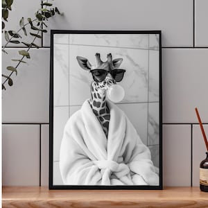 May include: Monochrome framed print of a giraffe wearing sunglasses and a white robe, blowing a bubble. The giraffe has a spotted pattern and is set against a marble tile background.