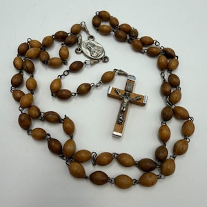 May include: A vintage rosary with oval wooden beads in varying shades of brown. The rosary features a silver-toned crucifix with a detailed depiction of Jesus and a silver medallion. The beads are strung on a metal chain.