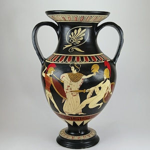 May include: A black ceramic amphora vase with a detailed painted scene of ancient figures. The vase features red, gold, and cream-coloured accents, with a decorative rim and handles. The vase is approximately 46 cm tall.