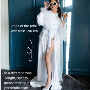 May include: White satin robe with feather trim on the sleeves and a matching belt. The robe's length with train is 190 cm. Text on the image: "For a different robe length, specify measurement in personalization."