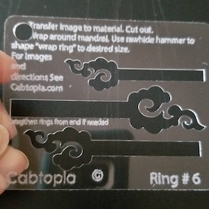 Può includere: Un modello in plastica trasparente con istruzioni per la creazione di un anello. Il modello presenta un design di tre nuvole stilizzate e il testo "Cabtopla" e "Ring #6".