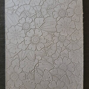 May include: A gray silicone mold with a detailed floral design. The mold features intricate flowers and leaves, perfect for creating decorative crafts. The mold is labeled "Cabtopia.com 100464".