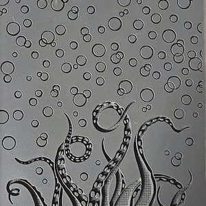 May include: A gray rubber stamp with a design of an octopus with tentacles rising from the bottom of the stamp. The octopus is surrounded by a pattern of circles, resembling bubbles. The text "Cabtopia.com © TM322" is printed at the bottom of the stamp.