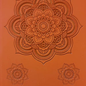 May include: Orange silicone mold with three detailed mandala designs. The largest design is a large, intricate mandala with multiple layers of petals and circles. The two smaller designs are smaller versions of the large mandala. The mold is labeled "Cabtopia.com 100545".