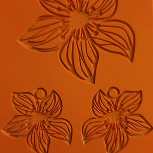 May include: Orange silicone mold with three flower designs. The top flower is larger than the two smaller flowers below. Each flower has a small circle at the top for hanging.