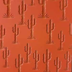 May include: Orange silicone baking mold with a repeating pattern of cactus silhouettes. The mold has the text "Cabtopia.com 100525" at the bottom.