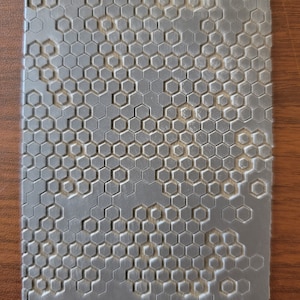 Puede incluir: Una baldosa rectangular gris texturizada con un patrón de panal de abeja. La baldosa tiene el texto "Cabtopia.com 100109" impreso en la parte inferior.