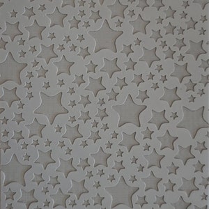 May include: A gray stencil featuring a pattern of various-sized stars. The stars are cut out, revealing a lighter background. The text "Cabtopia.com 100135" is printed at the bottom.