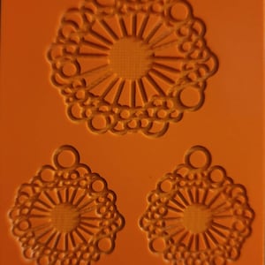 May include: Orange mold with three decorative pendant designs. The designs feature a central sunburst pattern surrounded by a circular, lacy border. The text "Cabtopia.com" and "100540" are visible.