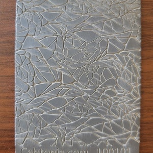 May include: A gray textured silicone mold with a cracked or broken pattern. The mold has the text "Cabtopia.com 100101" printed on the bottom.
