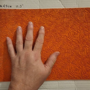 May include: Orange silicone sheet with a raised rose pattern. The sheet measures 11.3 inches by 8.3 inches. A hand is placed on the sheet to show the size.