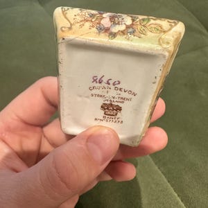 May include: A small, rectangular Crown Devon ceramic piece with floral and leaf designs in pink, blue, and green. The base features the text "CROWN DEVON STOKE-ON-TRENT ENGLAND" and "BANFF R.N. 577373".