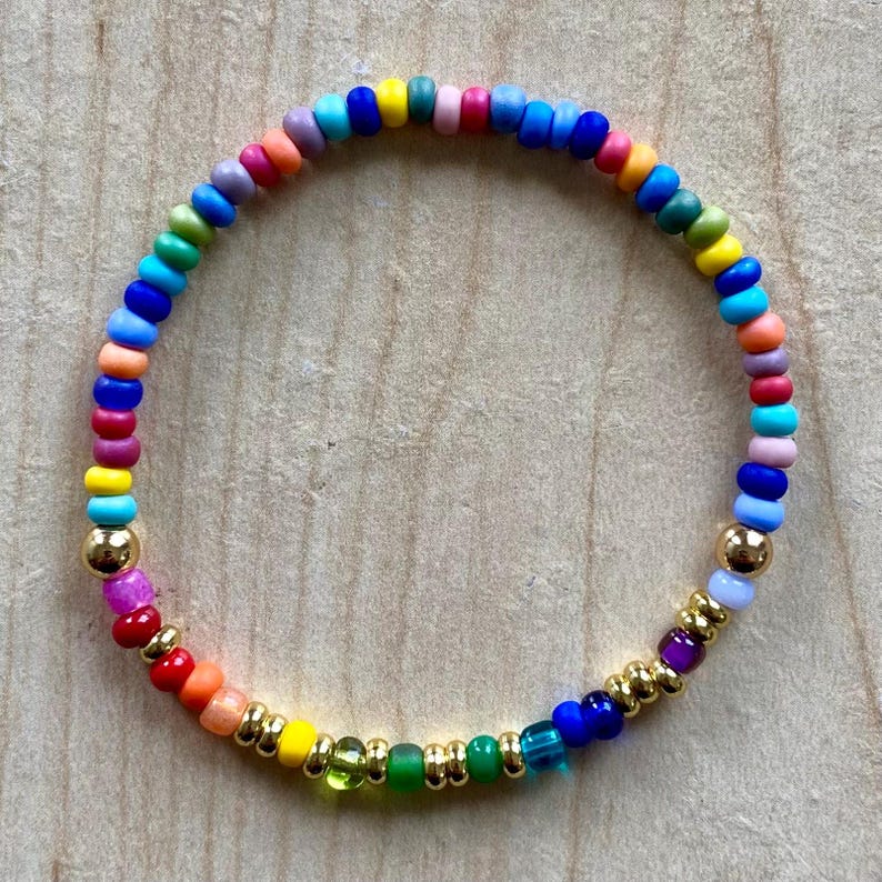 Pu&ograve; includere: Un braccialetto di perline multicolore con un arcobaleno di colori, tra cui rosso, arancione, giallo, verde, blu e viola. Perline color oro sono incorporate nel design. Un accessorio vivace.