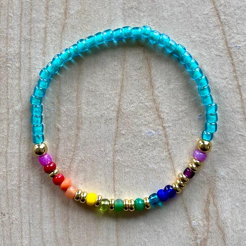 Pu&ograve; includere: Un braccialetto di perline colorate con un design arcobaleno, che include perline rosse, arancioni, gialle, verdi, blu e viola, con perline color oro. La maggior parte del braccialetto &egrave; realizzata con piccole perline turchesi. Un accessorio vivace.