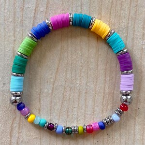 Puede incluir: Una colorida pulsera con un arcoíris de cuentas planas y redondas separadas por espaciadores metálicos plateados. La pulsera incluye tonos de rosa, azul, verde, amarillo y morado. Las cuentas están ensartadas en un cordón flexible.
