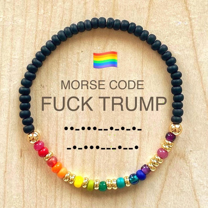 Pu&ograve; includere: Un braccialetto di perline con una fascia nera e una sezione arcobaleno. Il braccialetto presenta il testo "MORSE CODE FUCK TRUMP" e una bandiera arcobaleno. Viene visualizzato anche il codice Morse del testo.