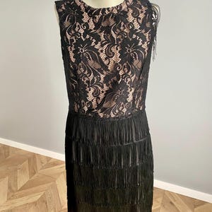 May include: A black sleeveless dress with a lace bodice and a fringed skirt, displayed on a mannequin. The lace bodice features a floral pattern, and the fringed skirt adds movement. The dress is a classic design, suitable for various occasions.