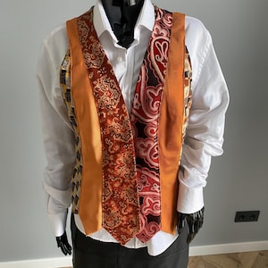 Puede incluir: Un chaleco único hecho de corbatas recicladas. El chaleco presenta un diseño de patchwork con varios patrones y colores, incluyendo naranja, marrón y telas estampadas. Se usa sobre una camisa blanca con cuello y una falda negra.