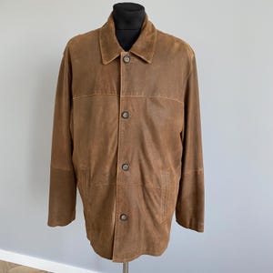 May include: A brown suede jacket with a collared neckline and button-down closure. The jacket has long sleeves and a classic design. The color is a warm, medium brown, and the jacket appears to be in good condition.