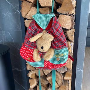 Peut inclure: Un sac à dos pour enfant avec un motif d'ours en peluche. Il présente un motif écossais rouge, du vichy vert et des pois rouges. L'ours en peluche est beige avec un nez noir et des yeux en bouton. Le mot "FELIX" est brodé sur le devant.