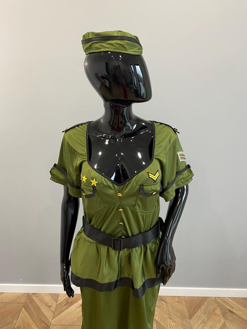 May include: An olive green military-style costume displayed on a mannequin. The outfit features a short-sleeved top with gold star and chevron details, a matching skirt, a black belt, and a peaked cap. The costume has black trim and gold buttons.