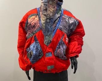 Könnte beinhalten: Eine rote Vintage-Skijacke mit bunten Mustereinsätzen an Schultern und Brust. Die Jacke hat einen hohen Kragen und Knöpfe. Die Jacke wird auf einer schwarzen Schaufensterpuppe präsentiert.