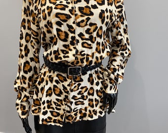 Op de afbeelding: Een button-down shirt met luipaardprint in bruin en zwart, gecombineerd met een zwarte riem en een zwarte rok. Het shirt heeft lange mouwen en een klassieke kraag. De riem is gevlochten met een rechthoekige gesp.