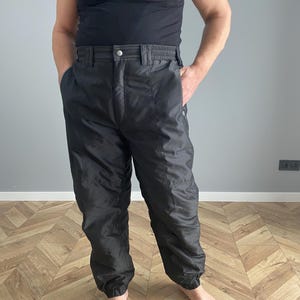 Può includere: Pantaloni da neve neri in nylon con elastico in vita e polsini alle caviglie. I pantaloni hanno una chiusura con bottoni e tasche. Progettati per attività con tempo freddo.