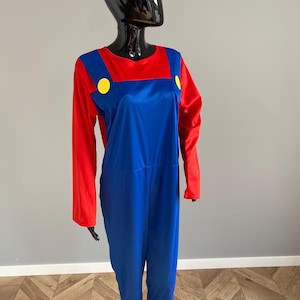 May include: A long-sleeved jumpsuit featuring a red shirt base with an attached blue overall overlay. The blue section includes two prominent yellow circular buttons positioned on the front straps, creating a distinct color-blocked appearance.
