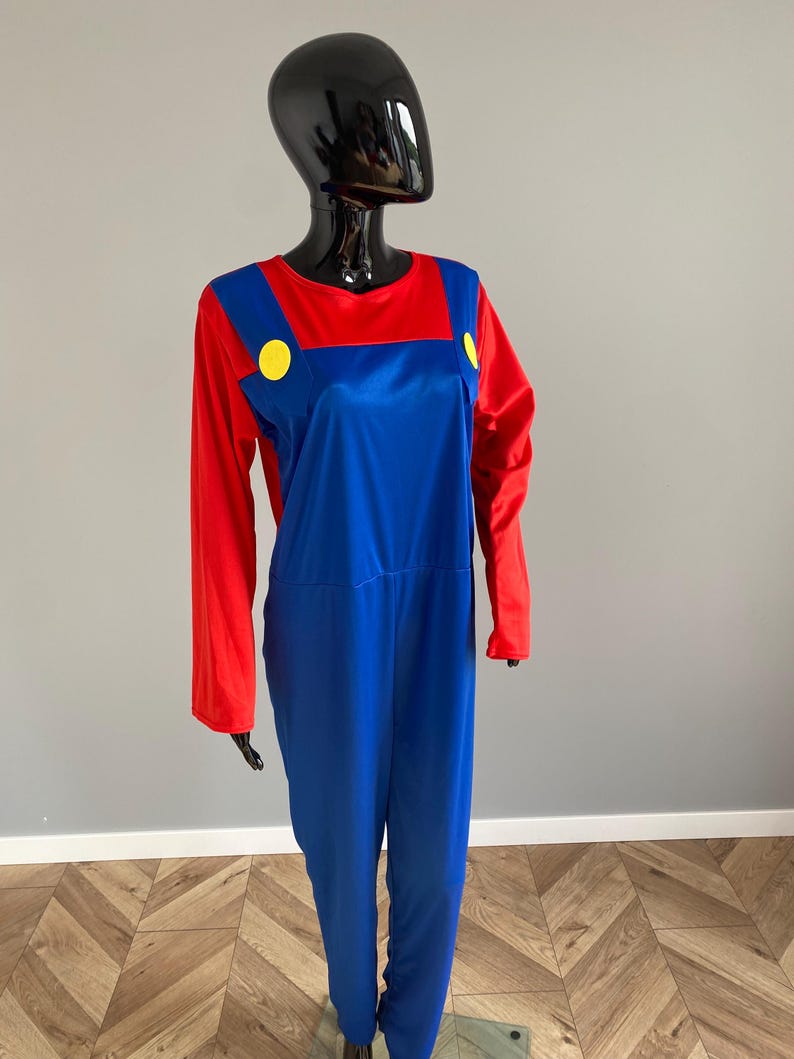May include: A long-sleeved jumpsuit featuring a red shirt base with an attached blue overall overlay. The blue section includes two prominent yellow circular buttons positioned on the front straps, creating a distinct color-blocked appearance.