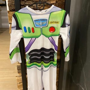 May include: A Buzz Lightyear costume with a white base, green accents, and the words "SPACE RANGER" and "LIGHTYEAR". The costume has long sleeves and a jumpsuit design, with a black and purple pattern on the front.