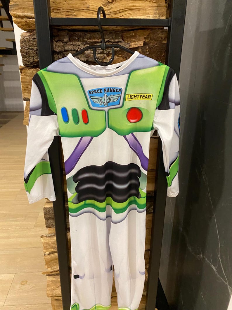 May include: A Buzz Lightyear costume with a white base, green accents, and the words "SPACE RANGER" and "LIGHTYEAR". The costume has long sleeves and a jumpsuit design, with a black and purple pattern on the front.