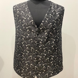 May include: A dark grey waistcoat featuring a repeating pattern of champagne glasses, shooting stars, and stars. The waistcoat has a V-neck, button closure, and two front pockets. It is displayed on a black mannequin.