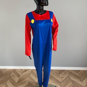 May include: A long-sleeved jumpsuit featuring a vibrant red shirt base with attached blue overalls. The blue overalls include two prominent yellow circular buttons at the chest straps. The garment is displayed on a black mannequin figure.