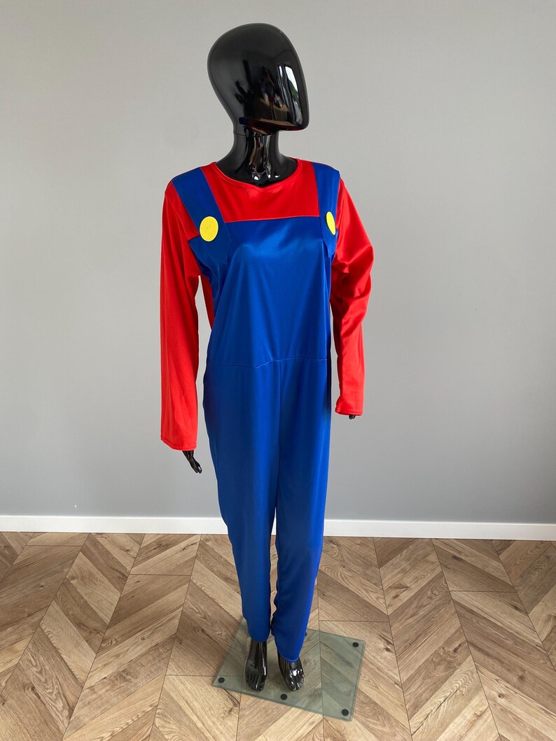 May include: A long-sleeved jumpsuit featuring a vibrant red shirt base with attached blue overalls. The blue overalls include two prominent yellow circular buttons at the chest straps. The garment is displayed on a black mannequin figure.