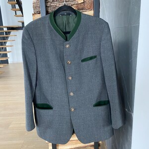 May include: A gray blazer with a green collar and pocket trim, hanging on a black hanger. The blazer has gold-colored buttons and a tailored fit. The jacket is displayed on a black metal rack.