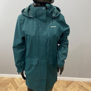 May include: A dark teal hooded rain jacket with a button-up front, two front pockets, and the brand name "Craghoppers" embroidered on the chest. The jacket is displayed on a mannequin.