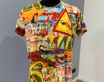 May include: A short-sleeved t-shirt with a vibrant, colorful print featuring cars, road signs, and graffiti-style text. The design includes orange, yellow, red, and green elements, creating a busy, eye-catching pattern. The shirt is displayed on a mannequin.