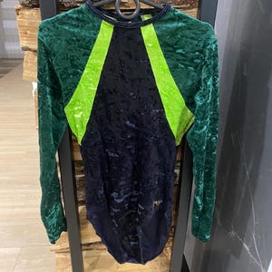Può includere: Body a maniche lunghe in verde, nero e verde neon. Il body ha una consistenza vellutata e uno scollo tondo. Il design presenta strisce verde neon sul petto e sulle spalle.
